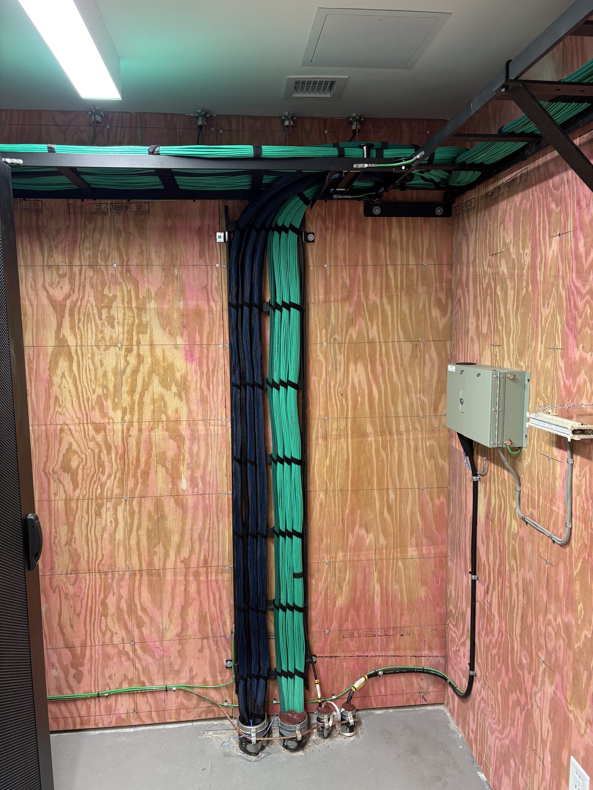 Green Cat6 bundles routed down a plywood backboard to floor penetrations