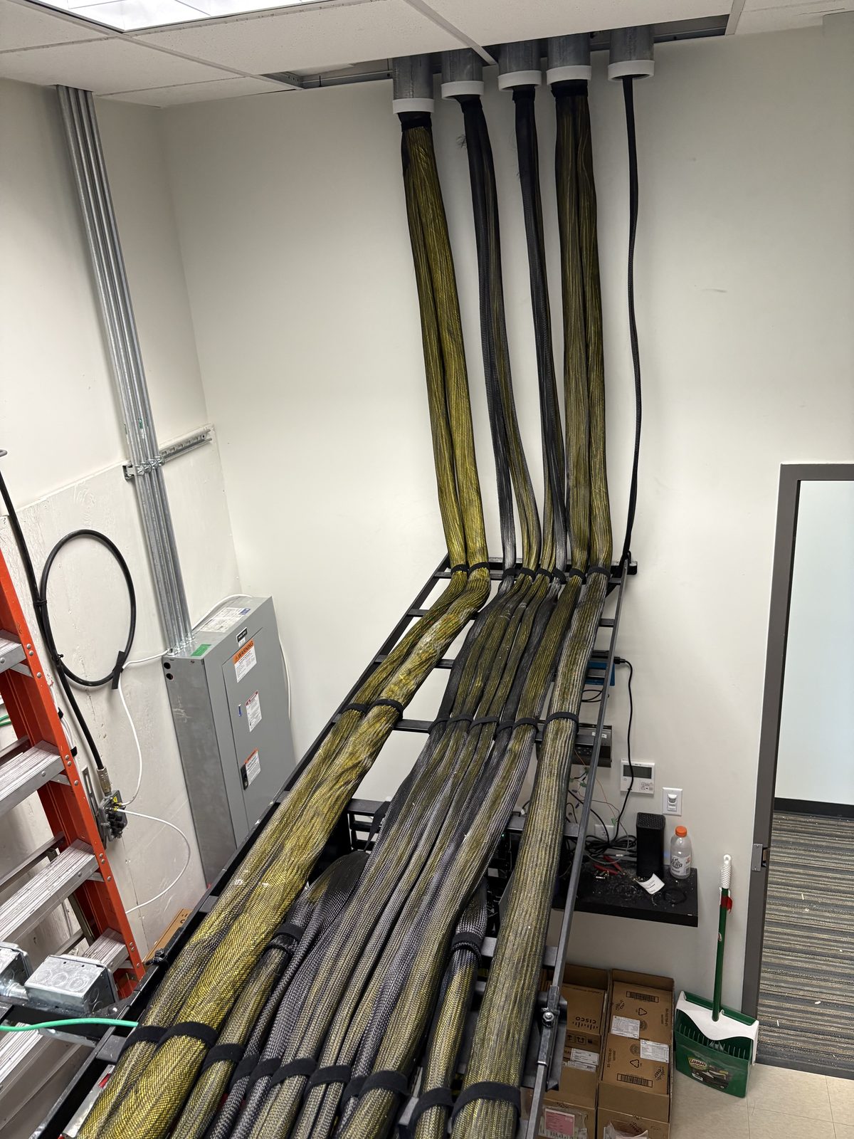 Sleeved riser cable bundles dropping from ceiling conduit onto a ladder rack