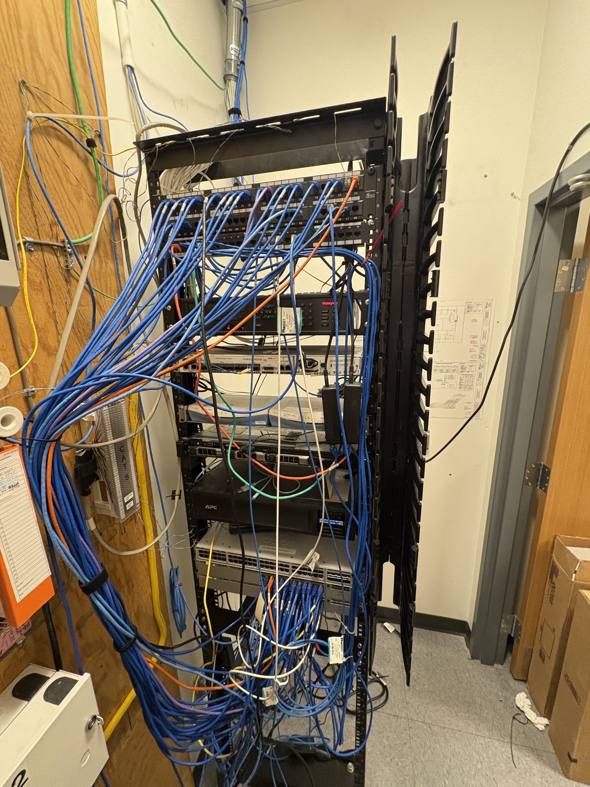 Wall-mounted rack overrun with tangled blue patch cables on a wood backboard