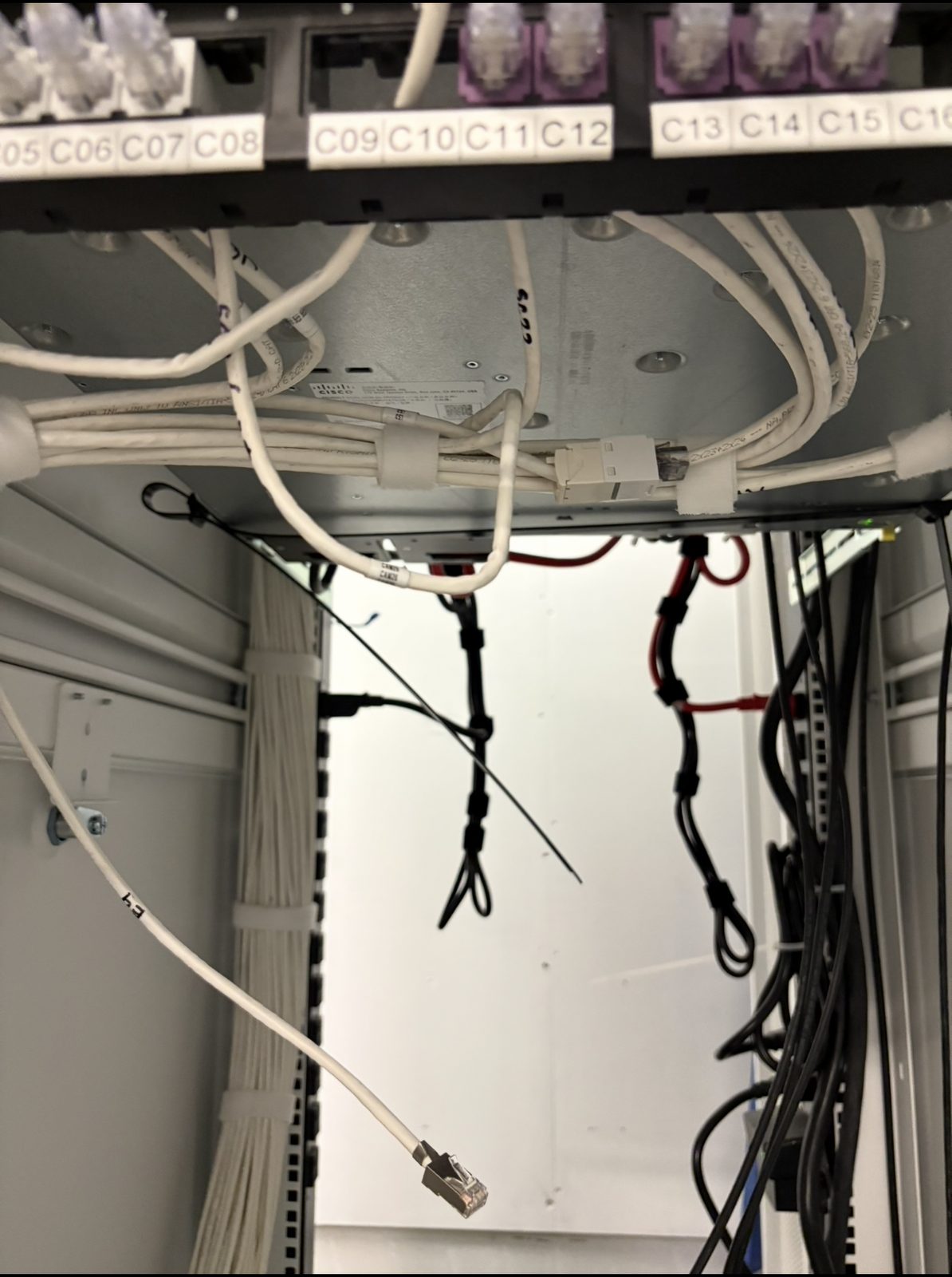 Under-rack view of disorganized patch cabling and loose service loops